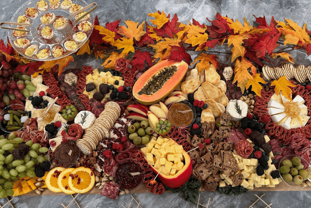 Fall grazing table with autumn leaves, papaya, salami roses, cheeses, crackers, grapes, berries, and deviled eggs